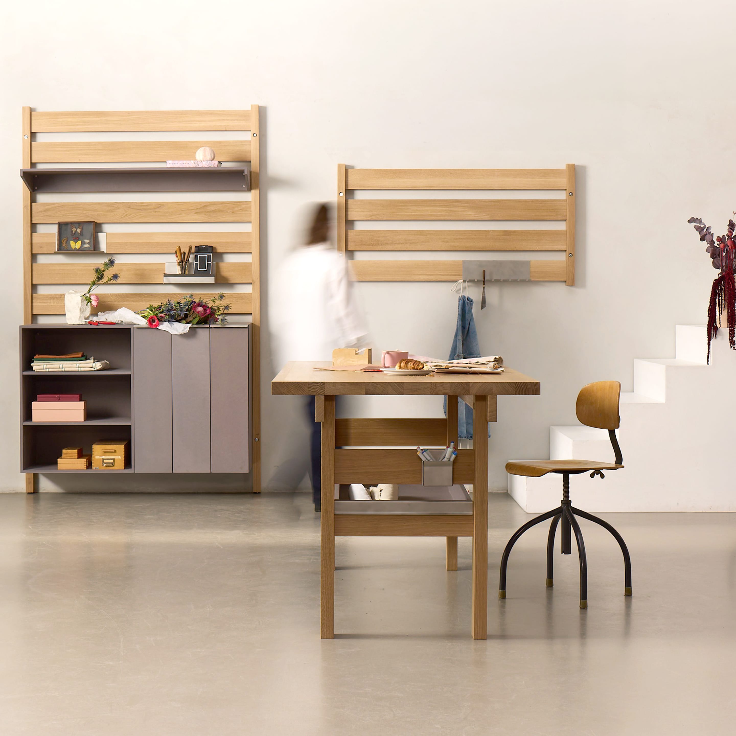Arbeitsraum mit Foyos-System: The Wall Wandmodule in Eiche, The Corpus Stauraum und The Bench als Arbeitstisch. Eine Person bewegt sich durch den Raum.