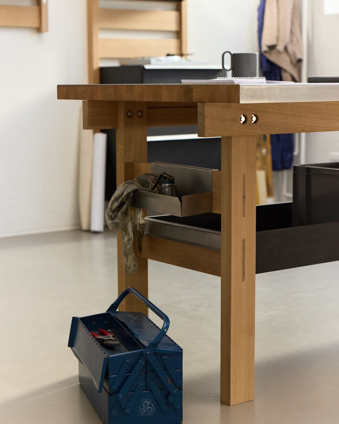 The Bench in Massivholz Eiche mit Edelstahl-Ablagen und Arbeitsplatte. Im Hintergrund ein Wohnraum, im Vordergrund ein klassischer Werkzeugkasten.